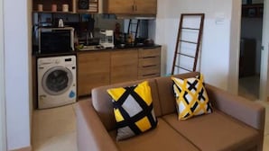 Un espace de vie compact comprenant un coin cuisine, un canapé avec des coussins à motifs et un lave-linge.