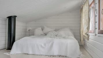 Een slaapkamer met een bed, kussens, een zwart cilindrisch voorwerp en een raam met gordijnen.
