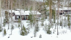 Eine Holzhütte, umgeben von schneebedeckten Bäumen, unter einem wolkenlosen Himmel.