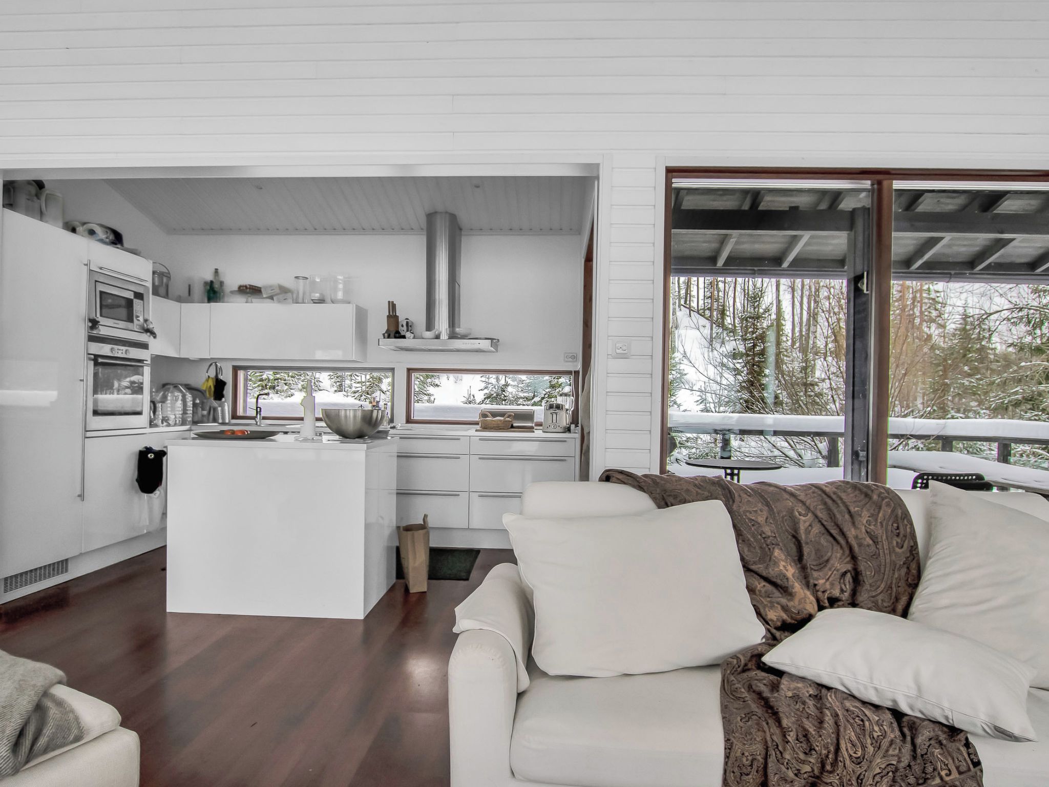Una cocina moderna con armarios blancos, una isla central y un amplio ventanal con vistas a un bosque.