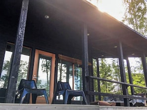 Ein überdachter Außenbereich mit Holzterrasse, zwei Plastikstühlen und einer Bank.