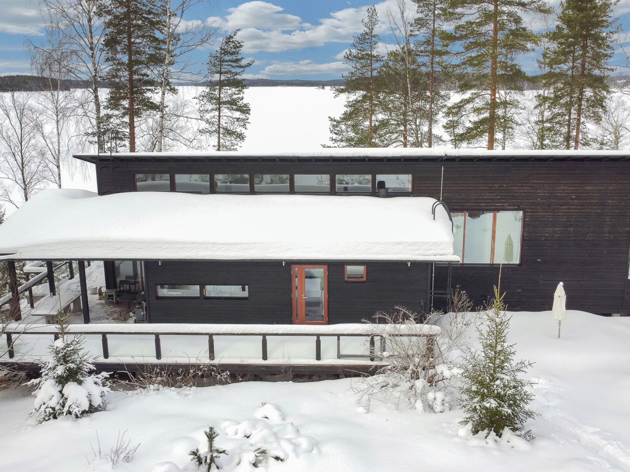 Una casa moderna de dos pisos con un porche cubierto y techo nevado.