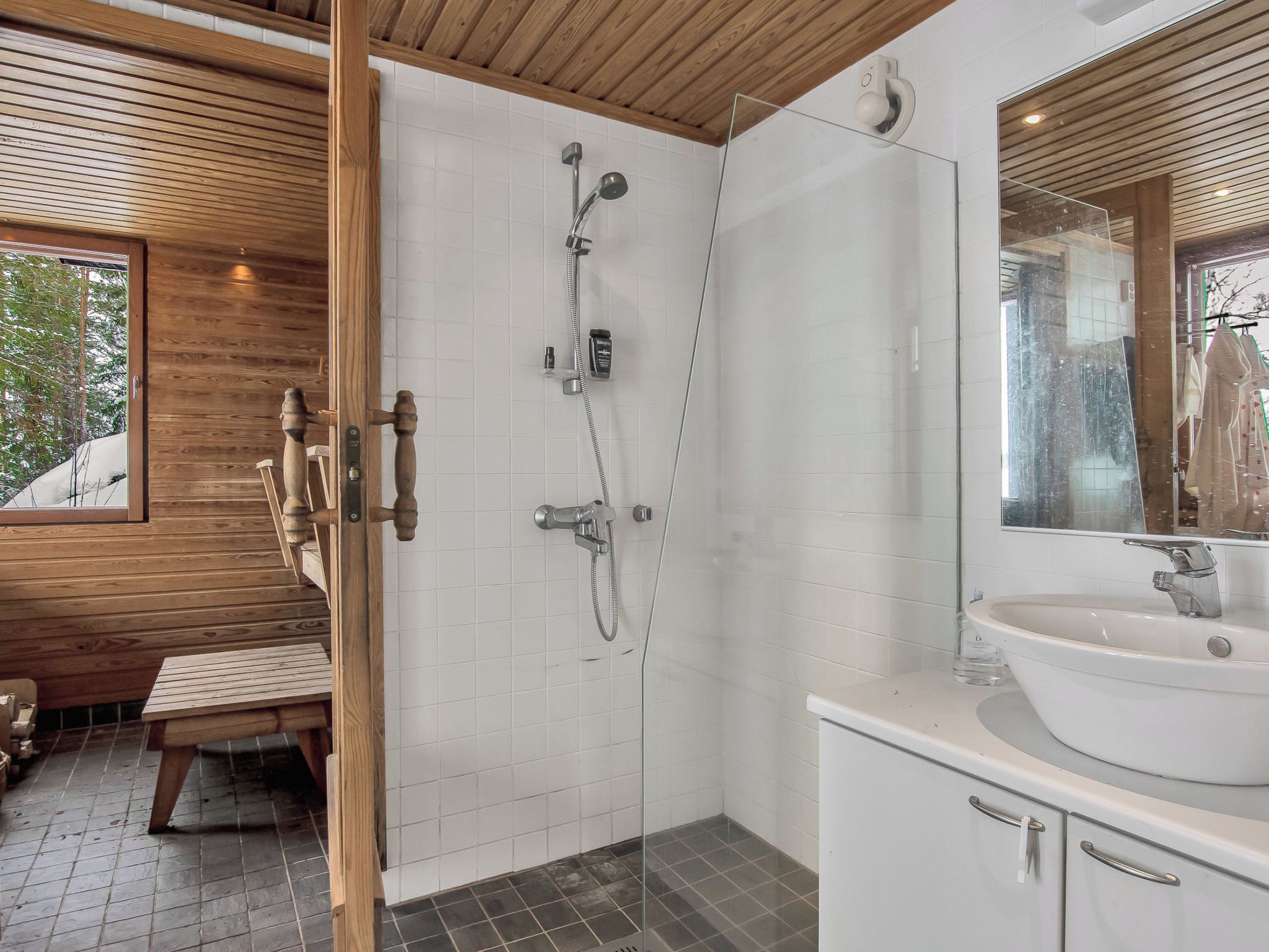 A modern bathroom with a glass shower enclosure, a white sink, and wooden accents.