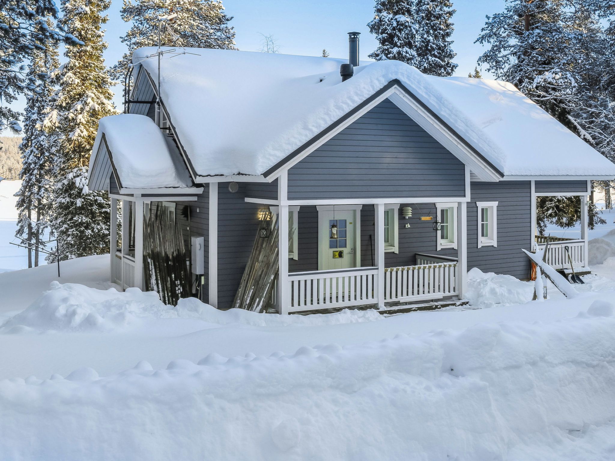 Ett tvåvåningshus med en inglasad veranda och en skorsten, omgivet av snö och träd.