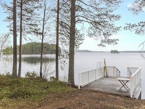 A wooden dock with a white railing, a table, and a chair, overlooking a calm lake with trees in the background. - Rantala by Interhome (Ranua)