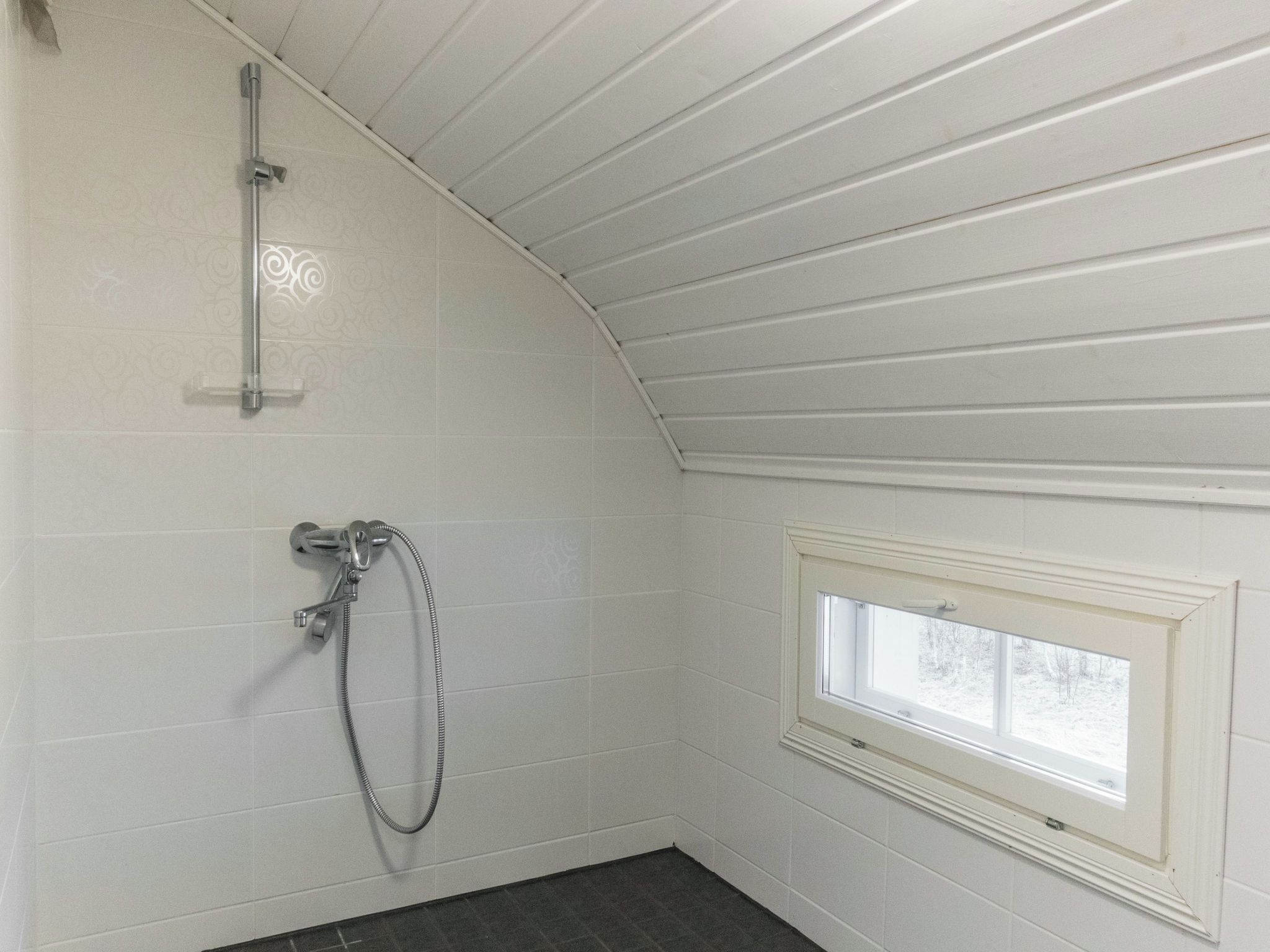 A bathroom with a shower, a window, and a sloped ceiling.