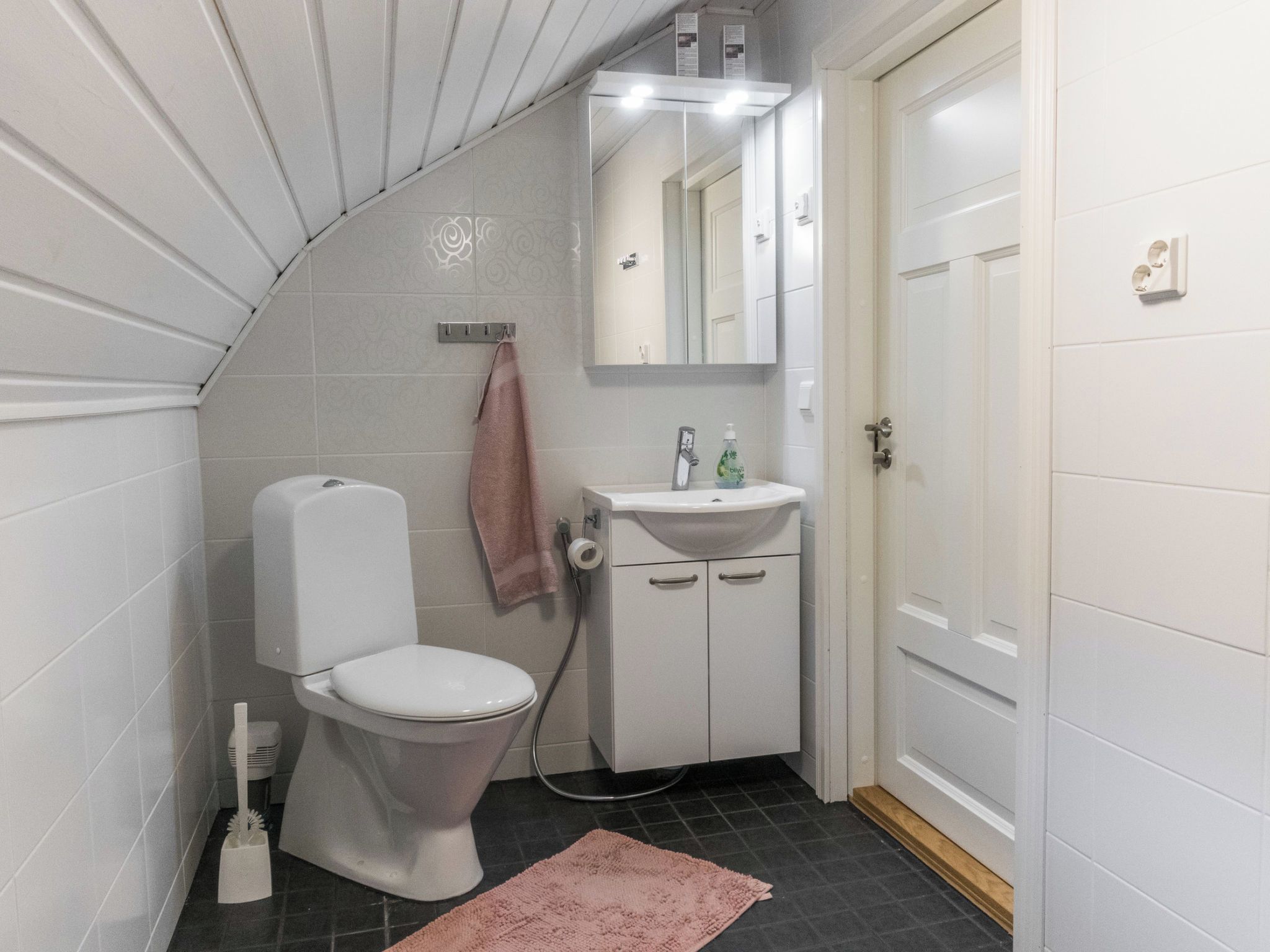 A bathroom with a toilet, sink, mirror, and a towel hanging on the wall.
