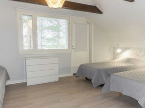 A bedroom with two beds, a window, a white dresser, and a sloped ceiling.