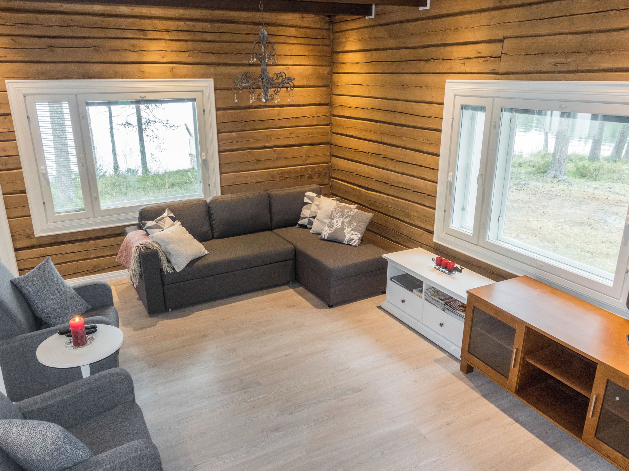 A cozy cabin interior with a sofa, a small table with a candle, and a view of the outdoors through large windows.
