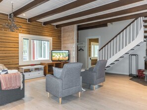 A modern living room with a wooden wall, a television, two grey armchairs, a white console table, and a staircase. - Rantala by Interhome (Ranua)