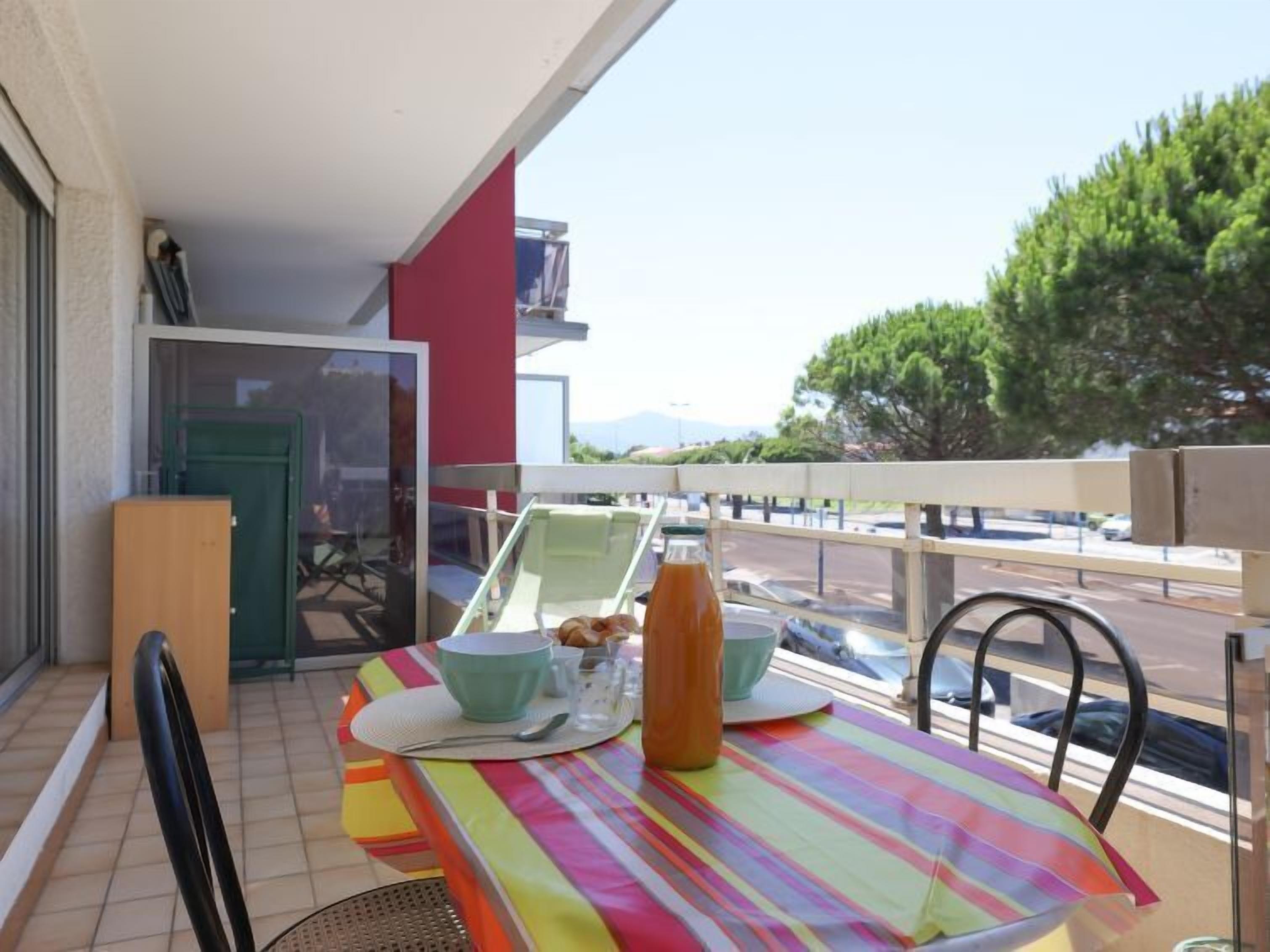 A balcony with a table set for two, a chair, a bottle, and a bowl.