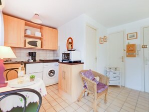 Een praktische keuken met een wasmachine, magnetron en een rieten stoel.