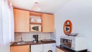 Kompakti keittiö, jossa on puukehikoiset kaapit, mikroaaltouuni, kahvinkeitin, pesukone ja leivänpaahdin.