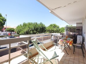 Een balkon met een tafel, stoelen, een barbecue en uitzicht op de straat en bomen.