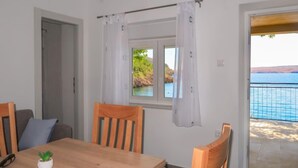 A room with a wooden table, chairs, a window with curtains, and a view of the sea. - Bajadera by Interhome (Jablanac)