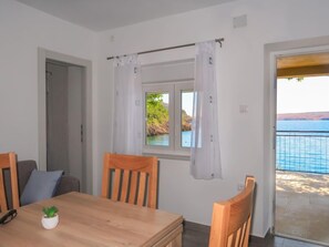 A room with a wooden table, chairs, a window with curtains, and a view of the sea. - Bajadera by Interhome (Jablanac)