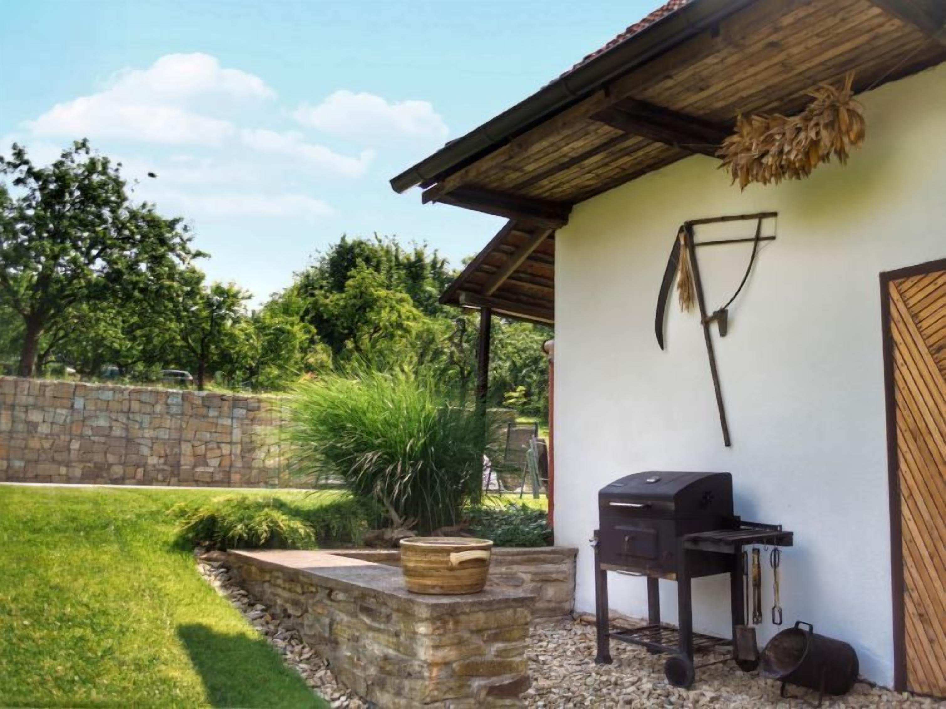 Un patio con un muro de piedra, un barril de madera, una parrilla y una puerta rústica.
