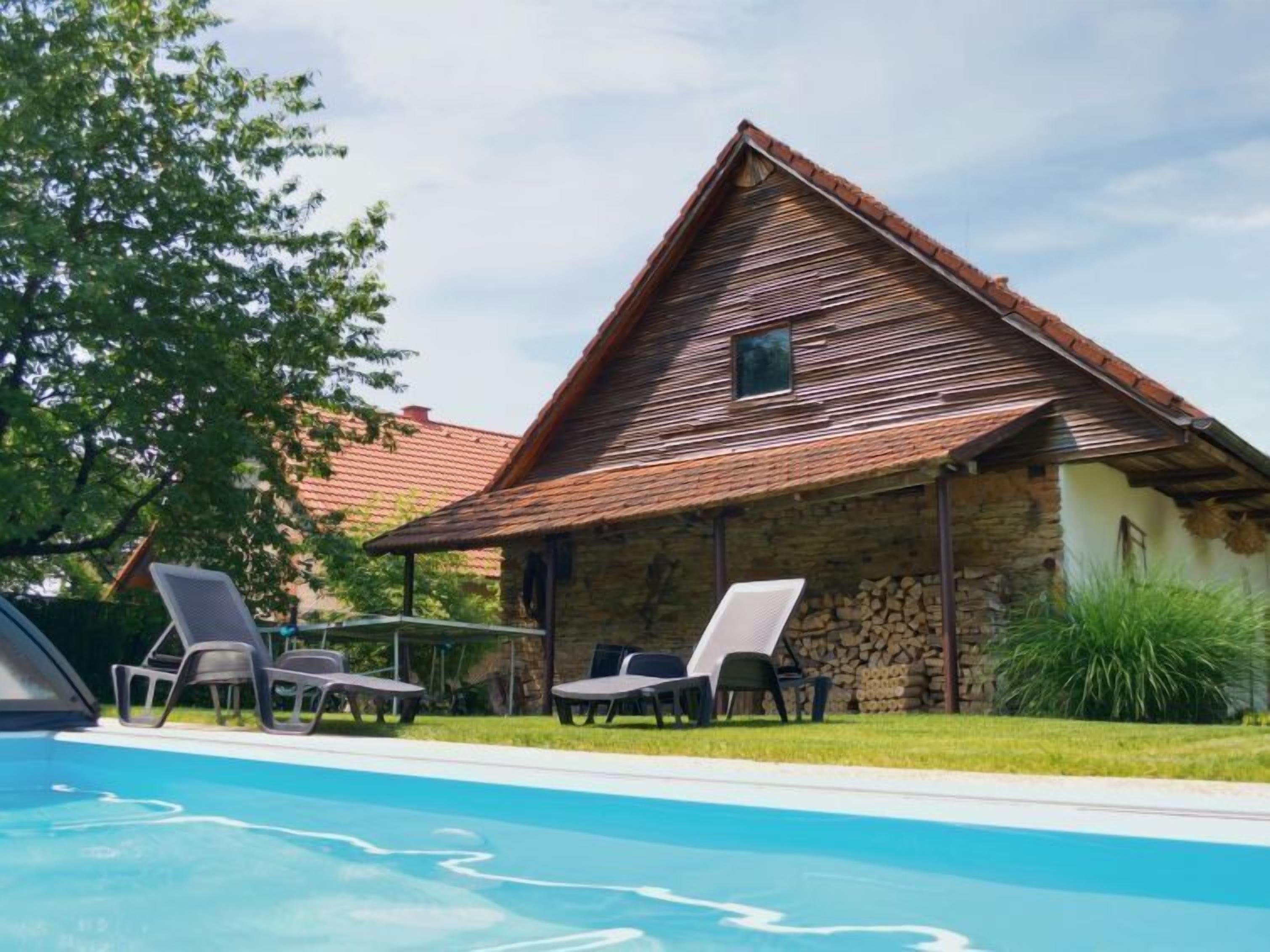 A stone building with a sloped roof and a pool area with lounge chairs.