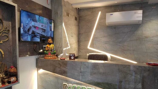 A reception area with a marble counter, a Buddha statue, and a television displaying multiple camera feeds. - Hotel Lotus Villa (Ahmedabad)
