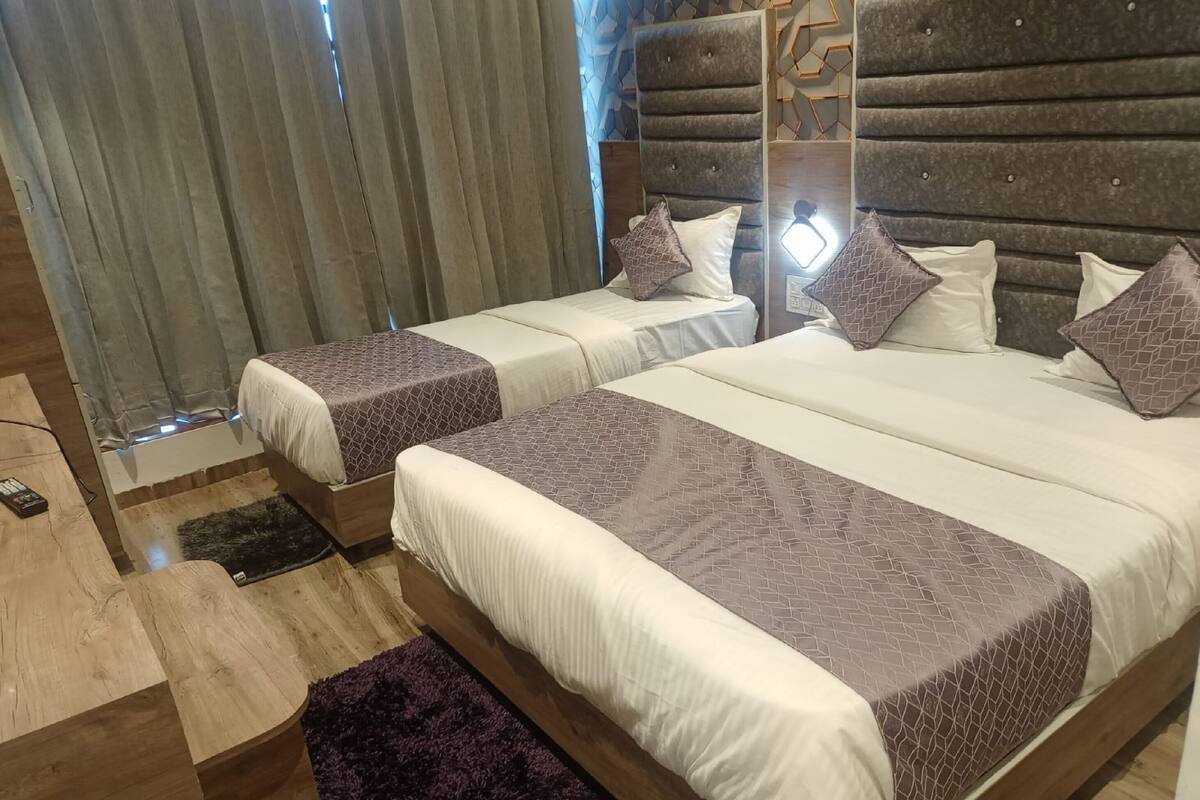 Una habitación de hotel moderna con dos camas, piso de madera, un escritorio pequeño y una ventana con cortinas.