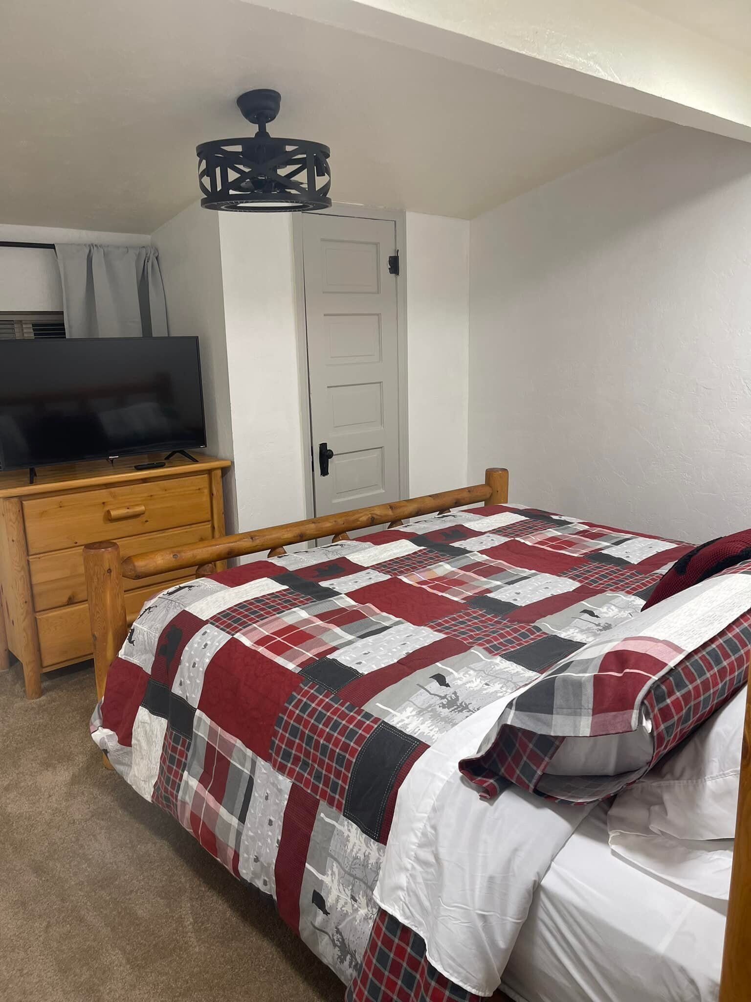 Ein Schlafzimmer mit einem Bett, einer Holzkommode, einem Fernseher und einer Tür.