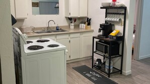 Een keuken met witte kasten, een fornuis, een spoelbak en een koffiehoek.