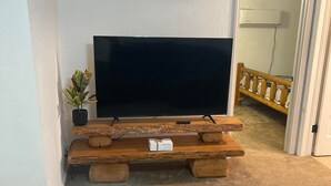 Een woonkamer met een flatscreen televisie op een rustieke houten bank, een kleine potplant en een lijst met een bordje aan de muur.