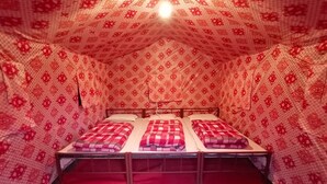 A room with three beds, each with a checkered blanket, and a red carpet. - Camp Awara Rishikesh (Narendranagar)