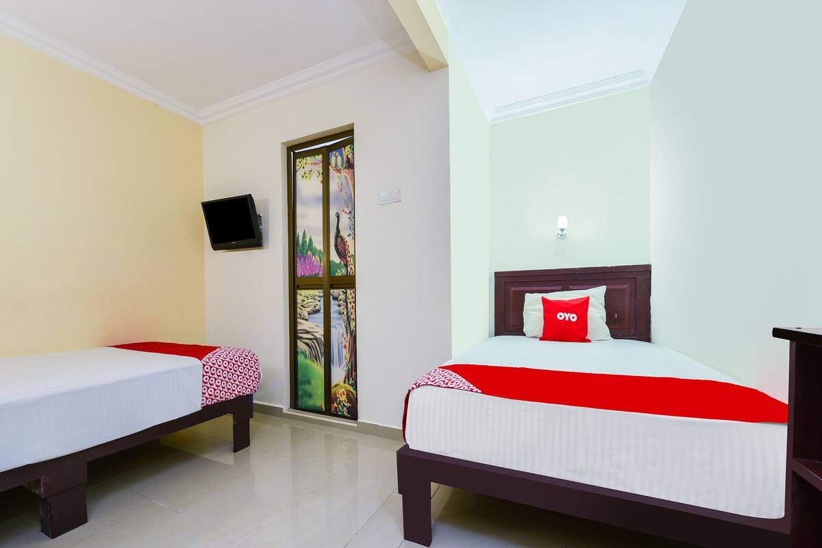 A hotel room with two single beds, a TV mounted on the wall, and a decorative door.