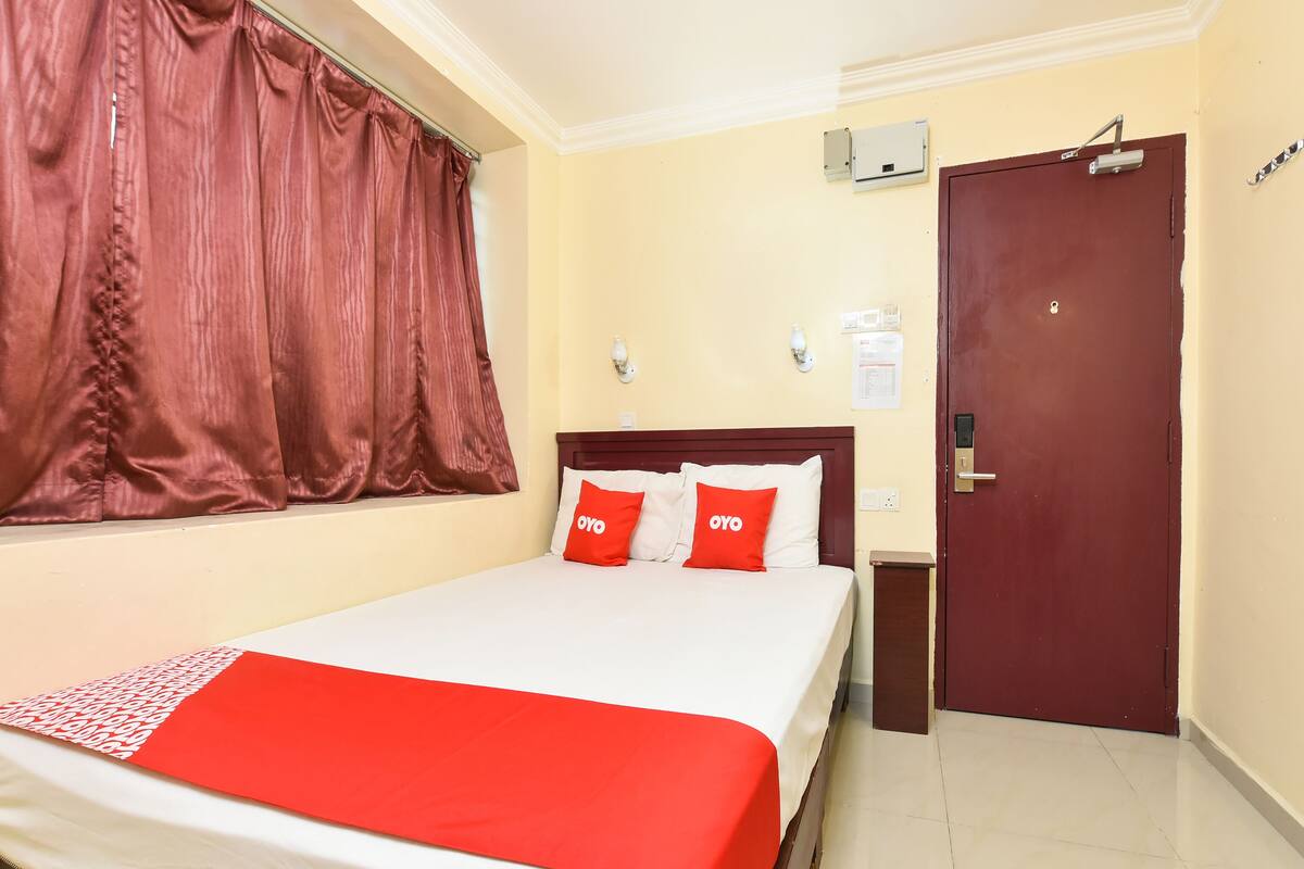 A hotel room with a bed, a red curtain, a wooden door, and a wall-mounted air conditioning unit.