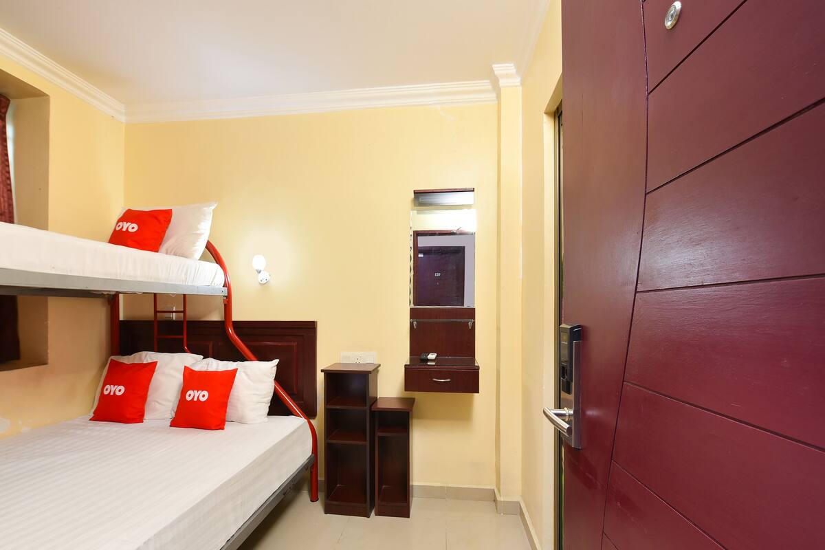 A hotel room with a bunk bed, a small desk, a mirror, and a wardrobe.