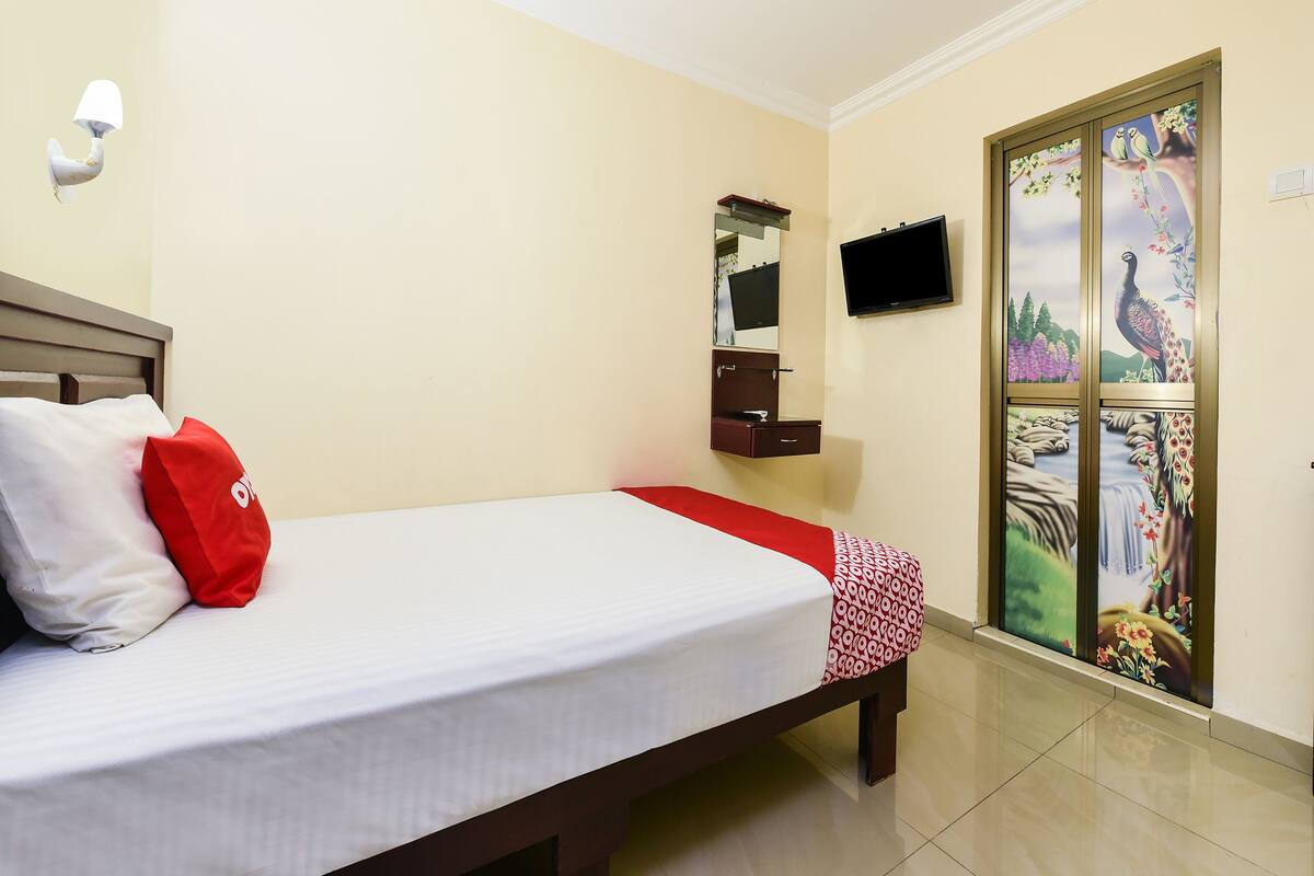A hotel room with a bed, a TV mounted on the wall, a small cabinet, and a sliding door with a nature-themed mural.