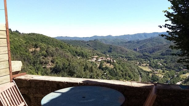 A balcony with a round table and two wooden chairs, overlooking a mountainous landscape with scattered buildings. - Studio with breathtaking views, nearby hiking and swimming trails (Chirols)