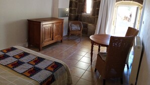 A cozy room with a wooden cabinet, a wicker chair, a dining table, and a quilt on the bed. - Studio with breathtaking views, nearby hiking and swimming trails (Chirols)