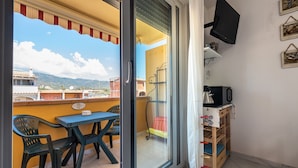A balcony with a table and chairs, a TV mounted on the wall, and a view of the mountains. - Apartment 'Maison Admas' with Mountain View, Balcony and Air Conditioning (Villasimius)
