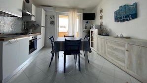 A compact kitchen with a dining area, a TV mounted on the wall, and a view through the door. - Apartment 'Maison Admas' with Mountain View, Balcony and Air Conditioning (Villasimius)