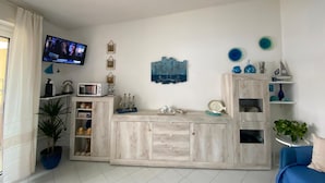 A modern living room with a TV, wooden cabinets, a blue sofa, and a potted plant. - Apartment 'Maison Admas' with Mountain View, Balcony and Air Conditioning (Villasimius)