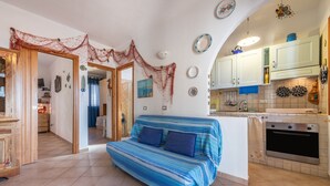 A living room with a sofa, kitchen area with cabinets, and a tiled floor. - Apartment 'Adriana's House' with Sea View, Private Terrace and Air Conditioning (Buggerru)