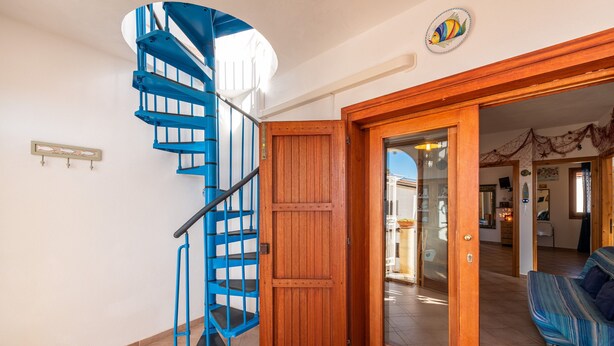 A spiral staircase with blue railings, a wooden door, and a sofa in a room with tiled flooring. - Apartment 'Adriana's House' with Sea View, Private Terrace and Air Conditioning (Buggerru)