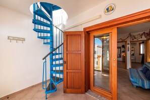 A spiral staircase with blue railings, a wooden door, and a sofa in a room with tiled flooring.