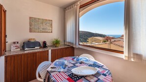 A dining area with a table set for two, a view of the sea, a map on the wall, and a kitchen counter with a toaster and a plant. - Apartment 'Adriana's House' with Sea View, Private Terrace and Air Conditioning (Buggerru)