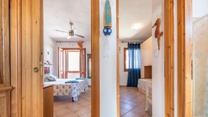 A room with a bed, a ceiling fan, a window with curtains, and a wooden door. - Apartment 'Adriana's House' with Sea View, Private Terrace and Air Conditioning (Buggerru)