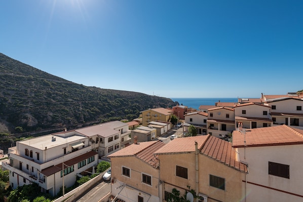 A coastal village with terracotta-roofed buildings, a clear sky, and a view of the sea.