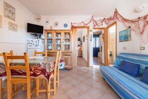 A dining area with wooden chairs and a table, a blue sofa, and a kitchen area with cabinets and a TV.