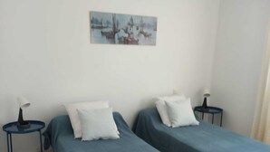 Ett rum med två enkelsängar, ett litet bord, en stol och en tavla på väggen.
