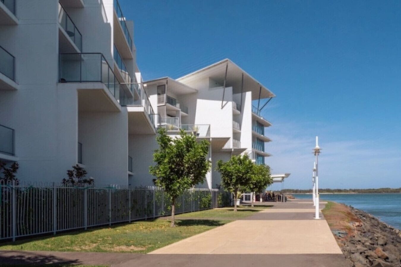 Een modern meerlaags gebouw met balkons, een verhard voetpad en uitzicht op zee.
