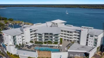 Et moderne hotel med central pool, flere altaner og udsigt til vandet.