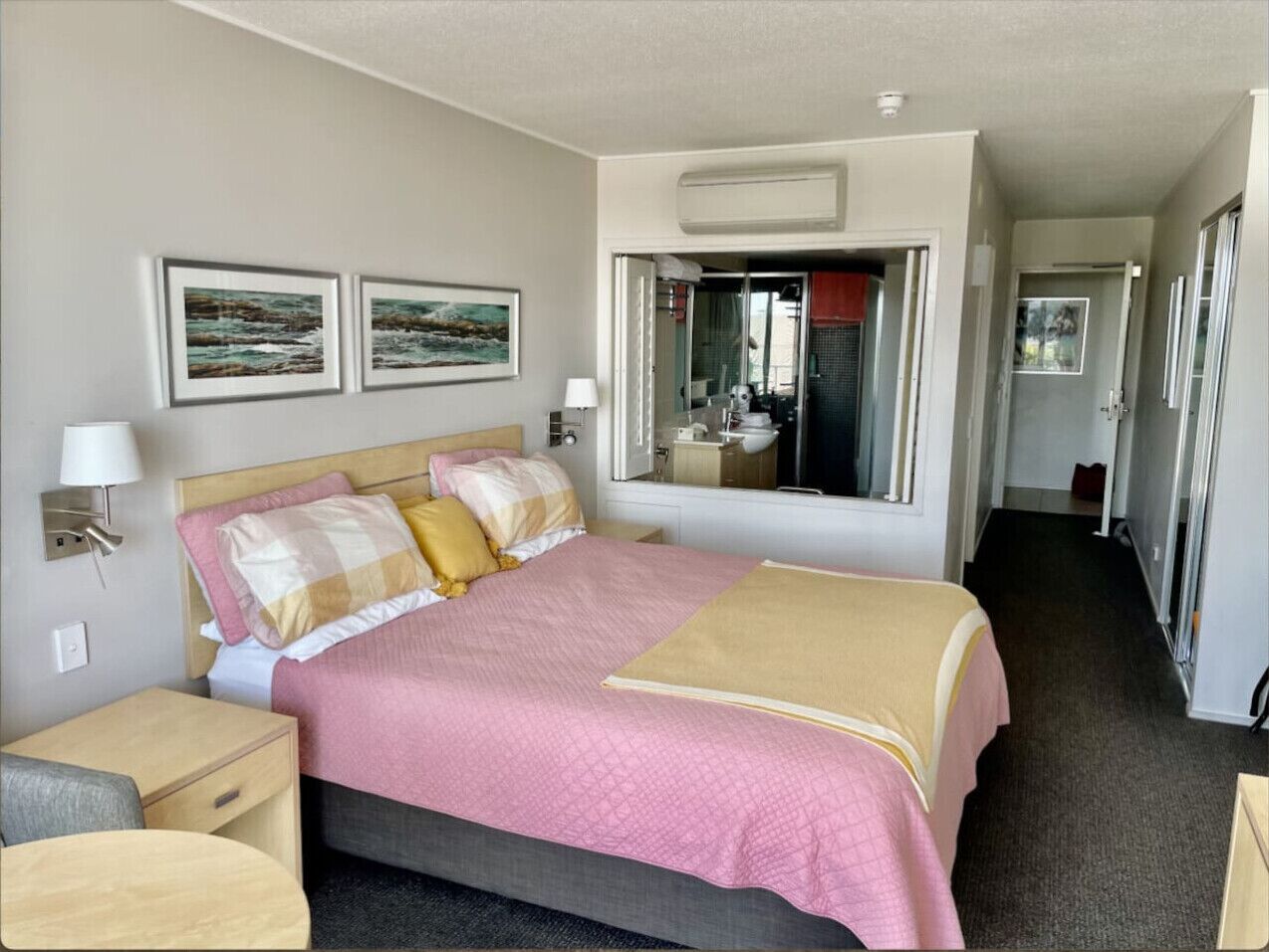 A hotel room with a bed, bedside tables, a mirror, and artwork on the wall.