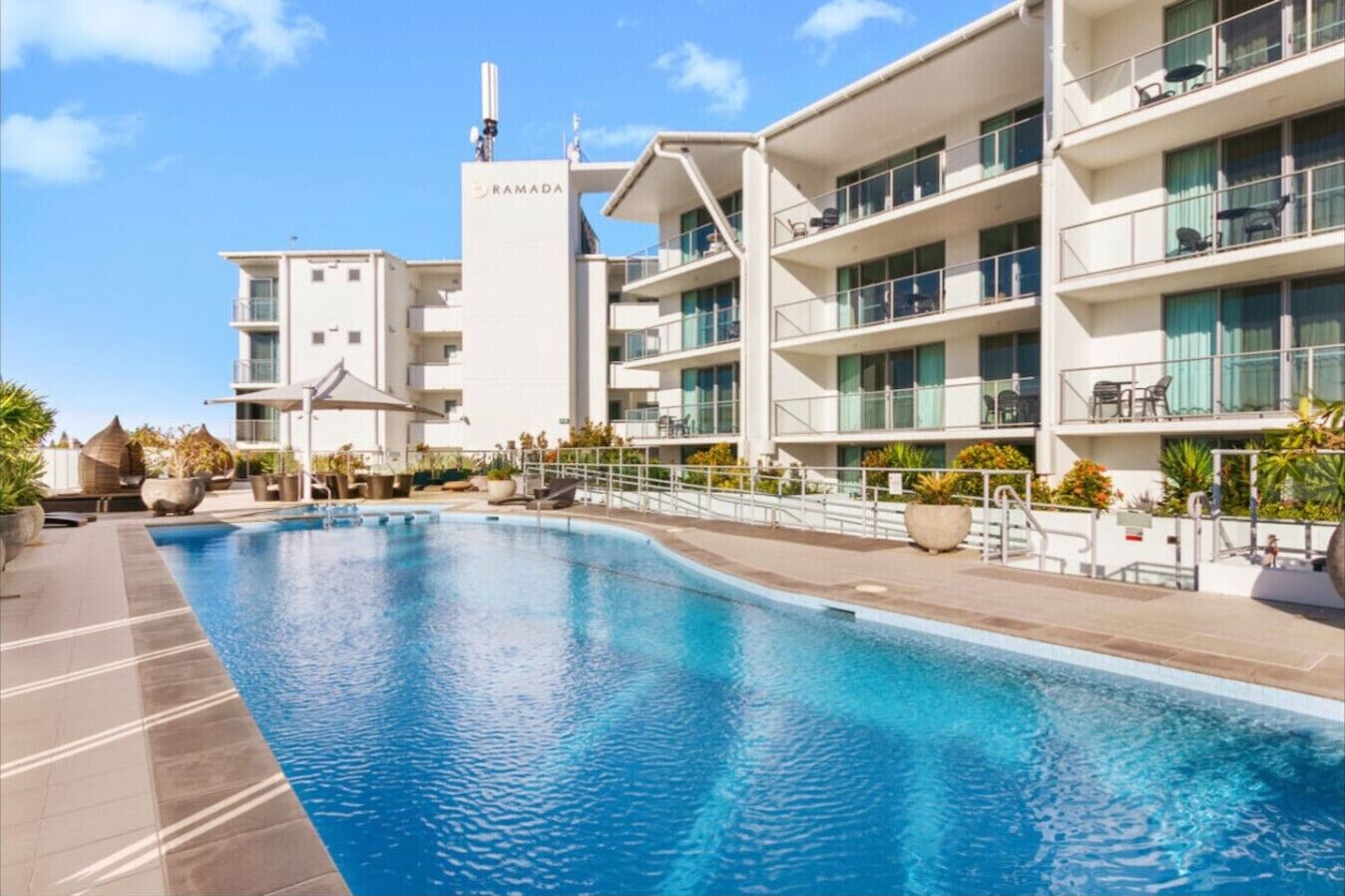 Un hôtel moderne doté d’une piscine, de nombreux balcons et offrant une vue sur un ciel dégagé.