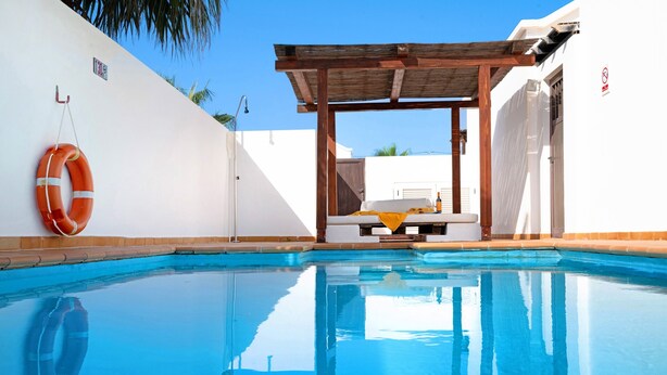 Une piscine agrémentée d’une pergola en bois, d’une bouée de sauvetage et d’un mur blanc avec une porte.
